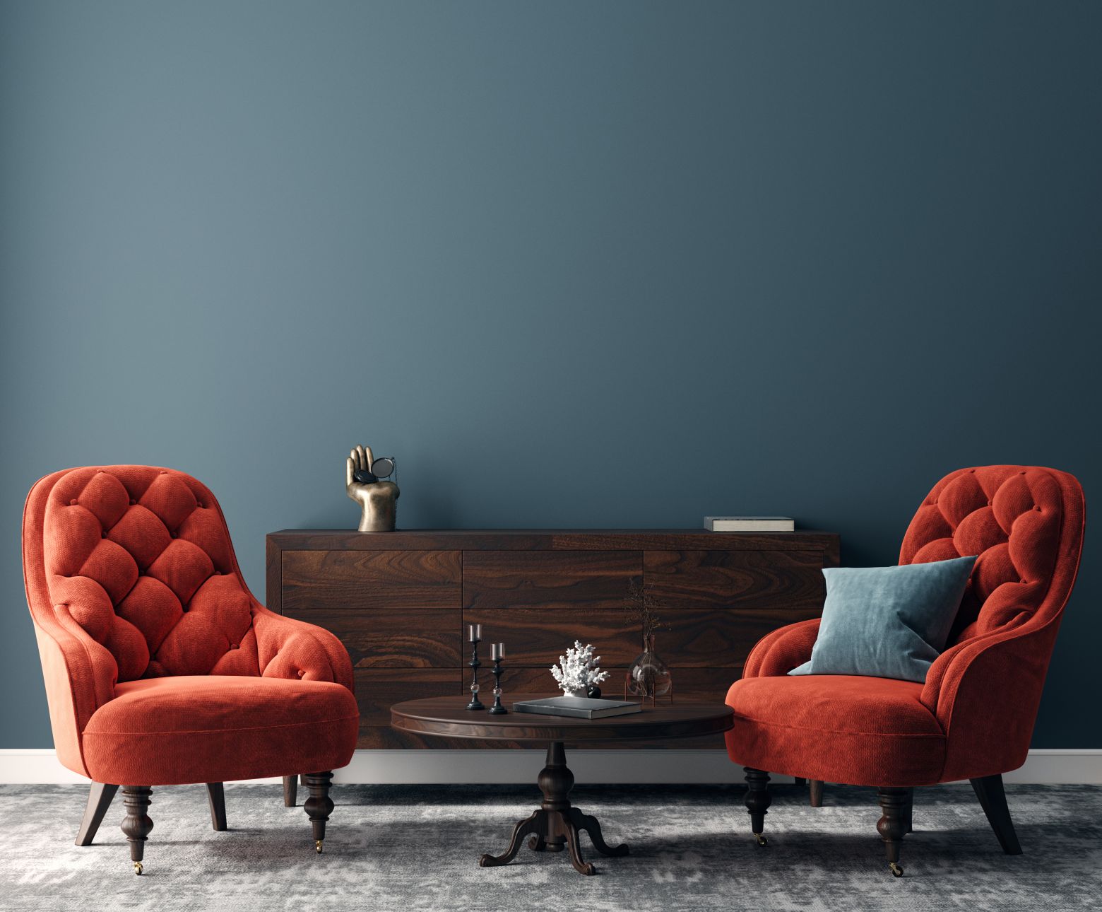 GettyImages-1285263796 Two red armchairs with a small table between them, a wooden sideboard, a decorative hand sculpture, and a teal wall in the background.