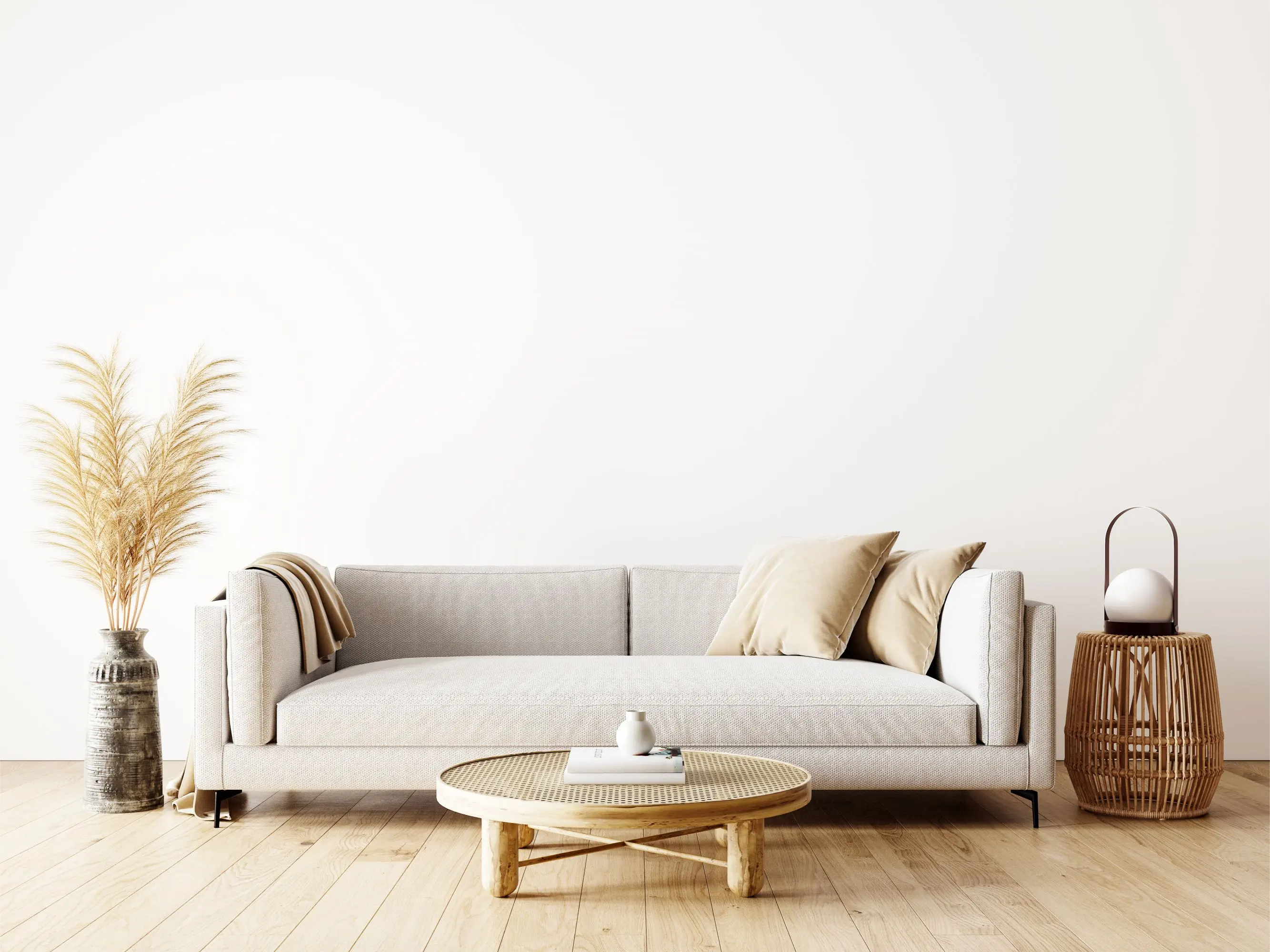 GettyImages-1310795181 Minimalist living room with a light gray sofa, two beige cushions, a small round wooden coffee table, decorative grass in a vase, and a wicker lantern on a wooden floor.