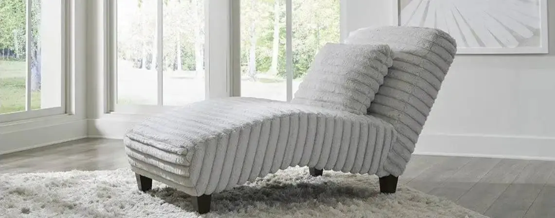 A gray, ribbed chaise lounge with a matching pillow sits on a fluffy rug